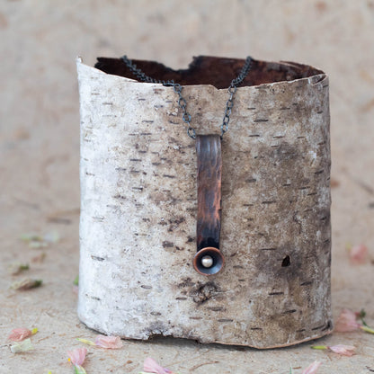 Hand-forged copper pendant necklace with rustic texture and silver accent, featuring a minimalist vertical bar design on oxidized chain for earthy artisan style.