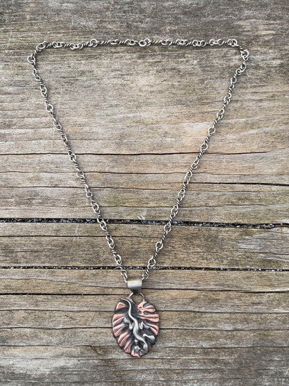 Full view of handcrafted sterling silver and copper pendant necklace featuring a sculpted lizard on a textured leaf background, with oxidized finish and nature-inspired artisan design. Hanging on a handmade sterling chain.