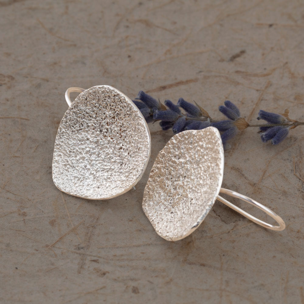 Silver textured earrings on a stone surface with lavender flowers