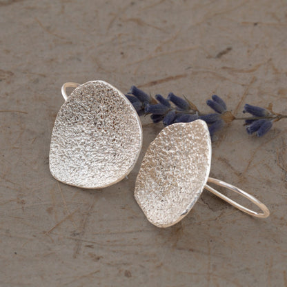 Silver textured earrings on a stone surface with lavender flowers