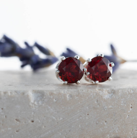 Pair of garnet gemstone stud earrings on a textured surface with blurred background