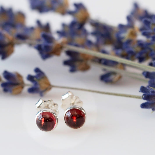 Round garnet stud earrings in sterling silver settings, styled with dried lavender on a white background.