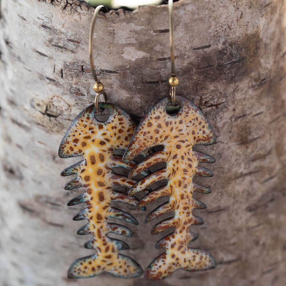 Fossil-style fish earrings on a wooden background