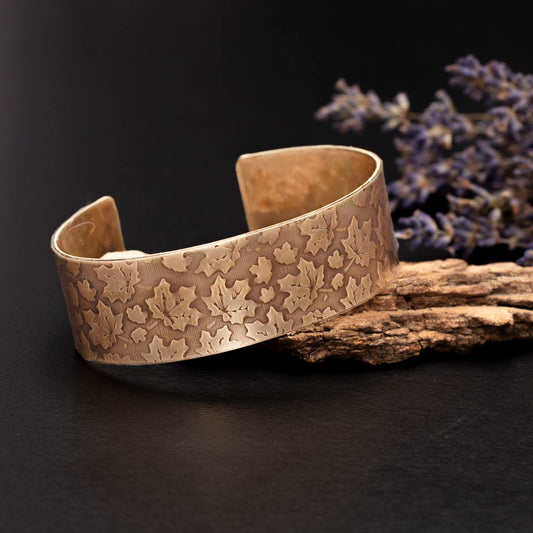 Etched brass cuff bracelet with a maple leaf pattern, photographed on wood with dried lavender accents.