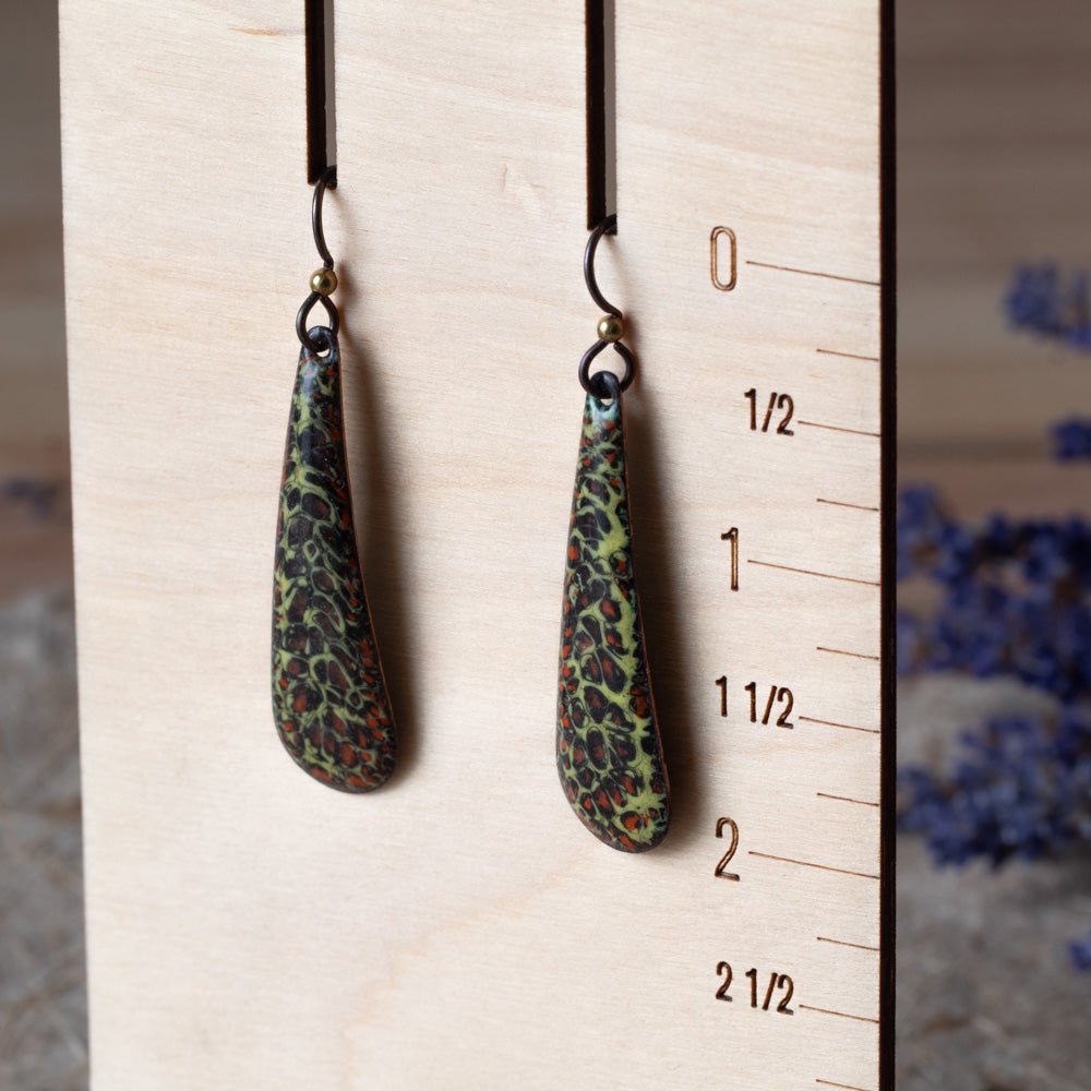 Green enamel teardrop earrings with dark organic texture, rusty orange details, and niobium ear wires.