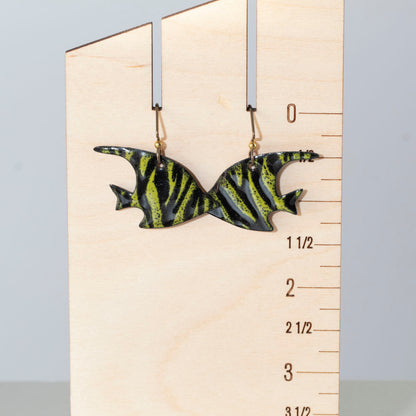 "Whimsical green and black enamel fish-shaped earrings with tiger-stripe pattern, displayed on a wooden ruler for scale – handmade by Divella Designs.