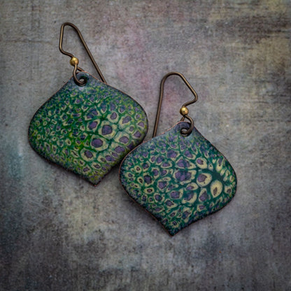 Handmade enamel earrings in green, yellow, and purple with lichen-inspired texture, diamond shape, and antique niobium ear wires on a stone background.
