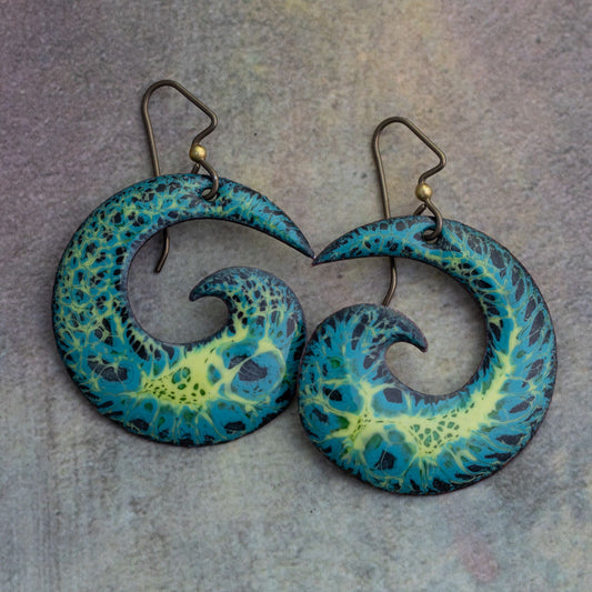 Handcrafted spiral enamel earrings in green, yellow, and blue with lichen-inspired texture and niobium ear wires, displayed on a stone background.