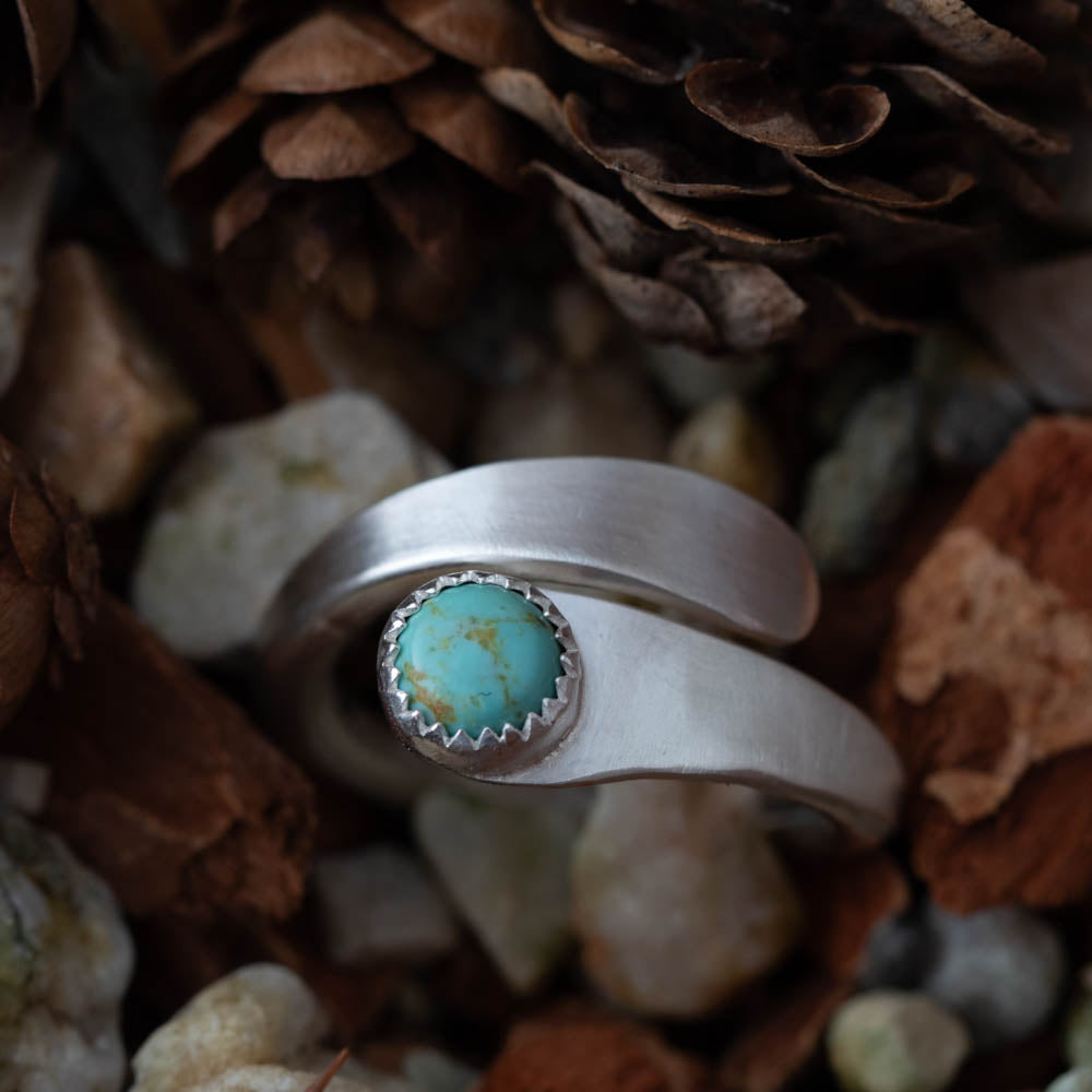 Silver ring with a kingman turquoise stone on a natural background of pine cones and stones