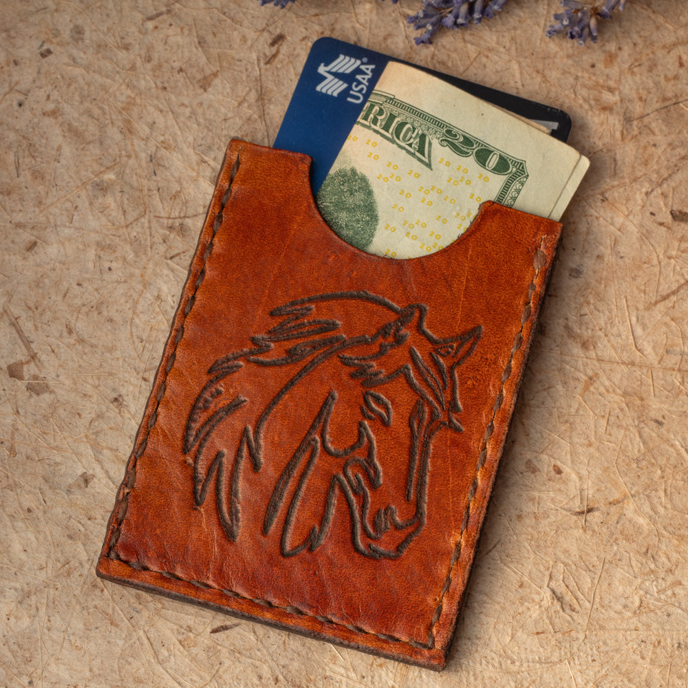 Handmade leather card case with embossed horse design. Compact size for cards or folded cash. Handmade in Vermont. Cash and credit card shown for scale 