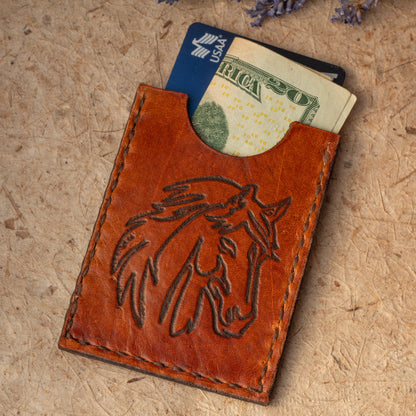 Handmade leather card case with embossed horse design. Compact size for cards or folded cash. Handmade in Vermont. Cash and credit card shown for scale 