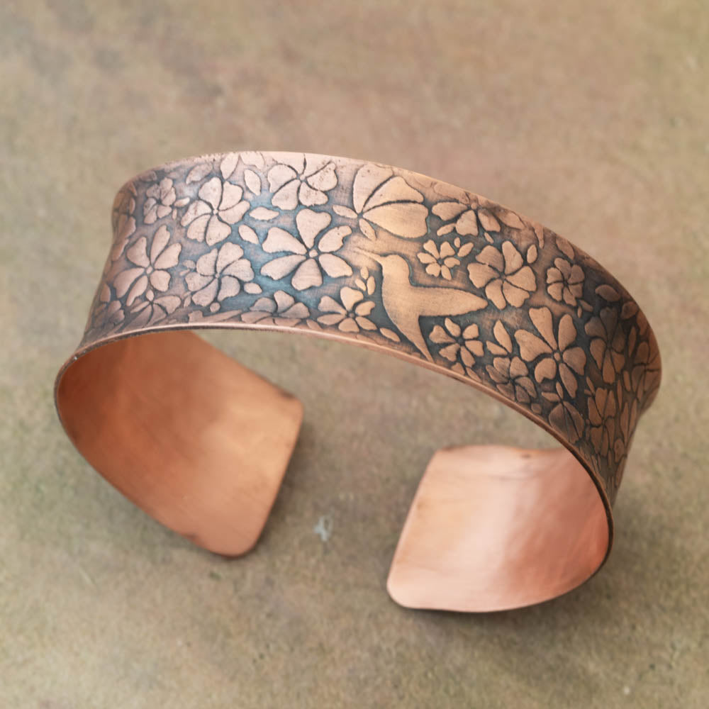 Copper bracelet with hummingbird and floral patterns on a textured surface
