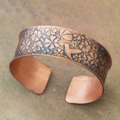 Copper bracelet with hummingbird and floral patterns on a textured surface