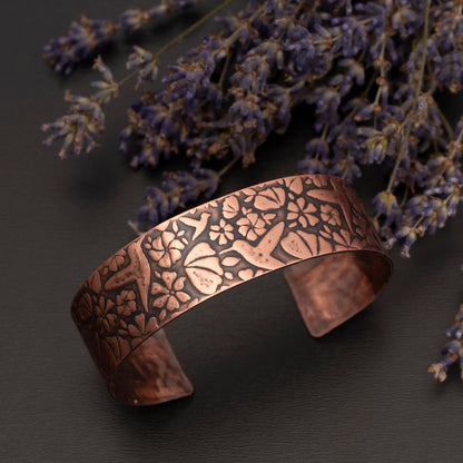 Etched copper cuff bracelet featuring a hummingbird pattern, displayed beside dried lavender on a dark background.