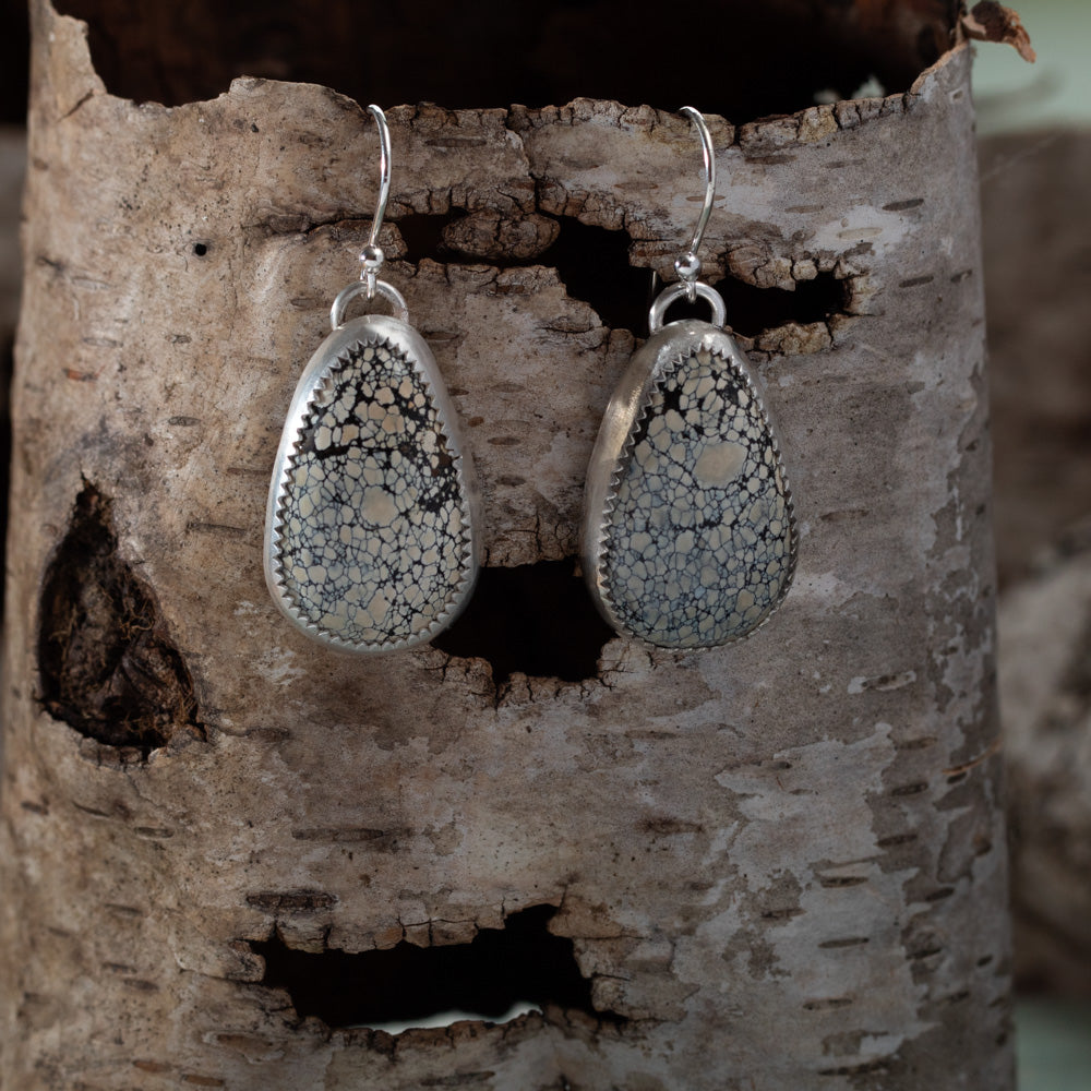 Teardrop-shaped silver earrings with a snowflake pattern hanging on a wooden surface.
