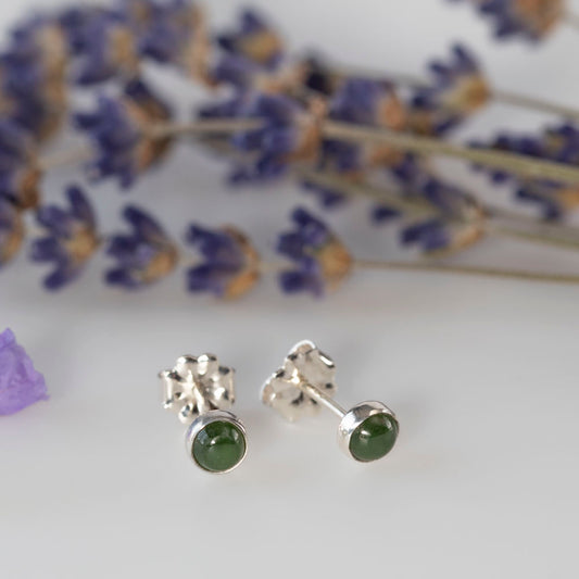 Side view of sterling silver stud earrings featuring round jade gemstones, styled with soft lavender in the background for a natural, elegant loo