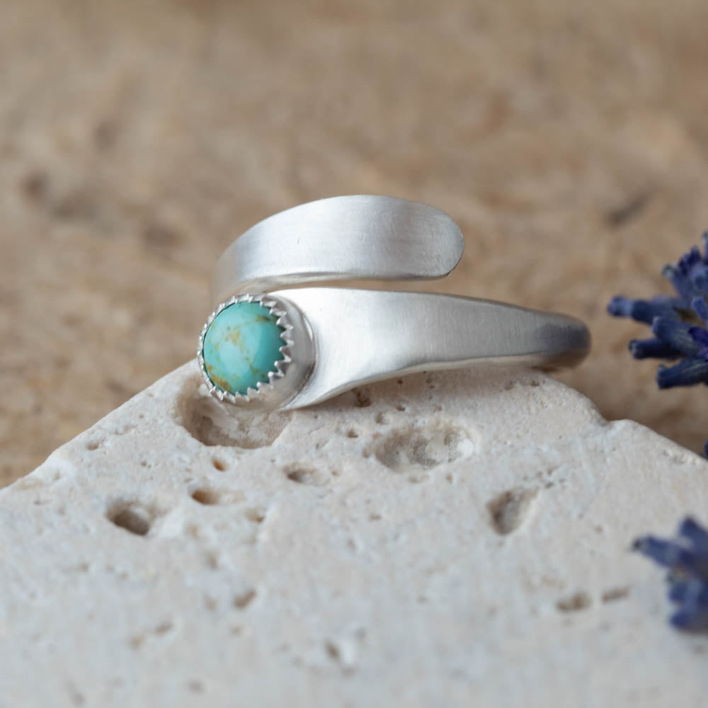 Adjustable sterling silver Kingman turquoise wrap ring photographed on a light stone surface