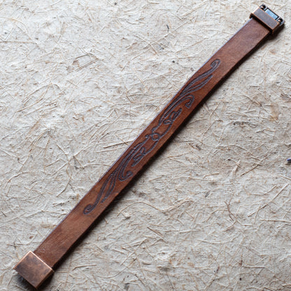Brown leather cuff with embossed design on a textured beige surface