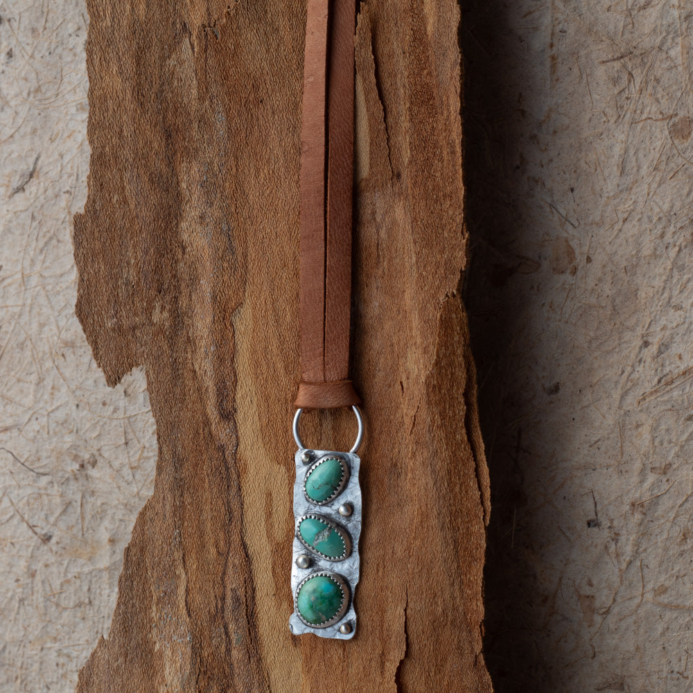 Necklace with turquoise stones and silver clasp on a brown leather strap against a textured stone background