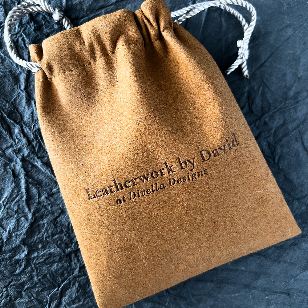 Brown leather drawstring bag with 'Leatherwork by David at Divella Designs' text on a dark textured surface.