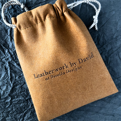 Brown leather drawstring bag with 'Leatherwork by David at Divella Designs' text on a dark textured surface.