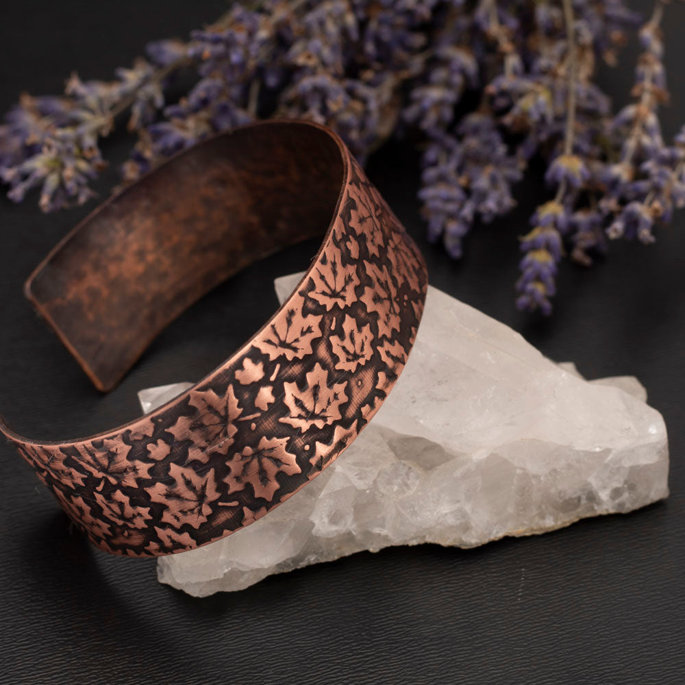 Etched copper cuff bracelet featuring a maple leaf pattern, displayed on a crystal with dried lavender on a dark background