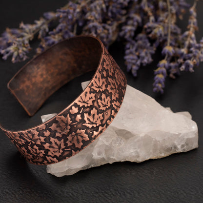 Etched copper cuff bracelet featuring a maple leaf pattern, displayed on a crystal with dried lavender on a dark background