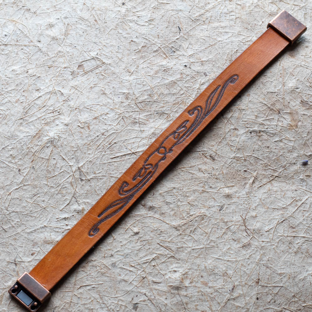 Brown leather cuff with decorative metal buckle on a textured surface