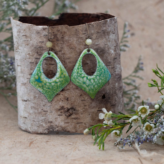 Handmade enamel earrings in a vibrant green and yellow crackle pattern, diamond shape with open center and glass bead accents. Artisan jewelry by Divella Designs, styled on birch bark with wildflowers – Meadowlight Enamel Earrings.