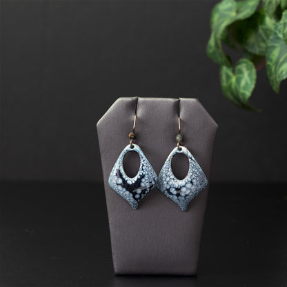 Handmade enamel earrings in a diamond shape with black and pale lilac patterning, open teardrop centers, niobium ear wires, and faceted gemstone beads.