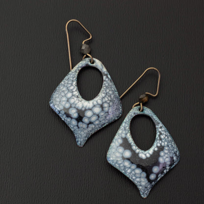 Handmade enamel earrings in a diamond shape with black and pale lilac patterning, open teardrop centers, niobium ear wires, and faceted gemstone beads.