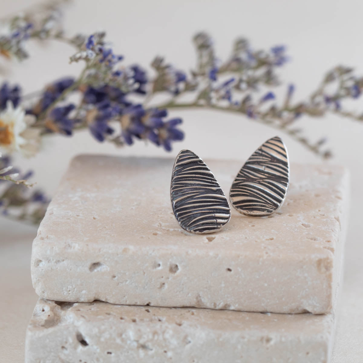 Handmade sterling silver teardrop stud earrings with etched line texture, featuring a minimalist nature-inspired design and oxidized finish.