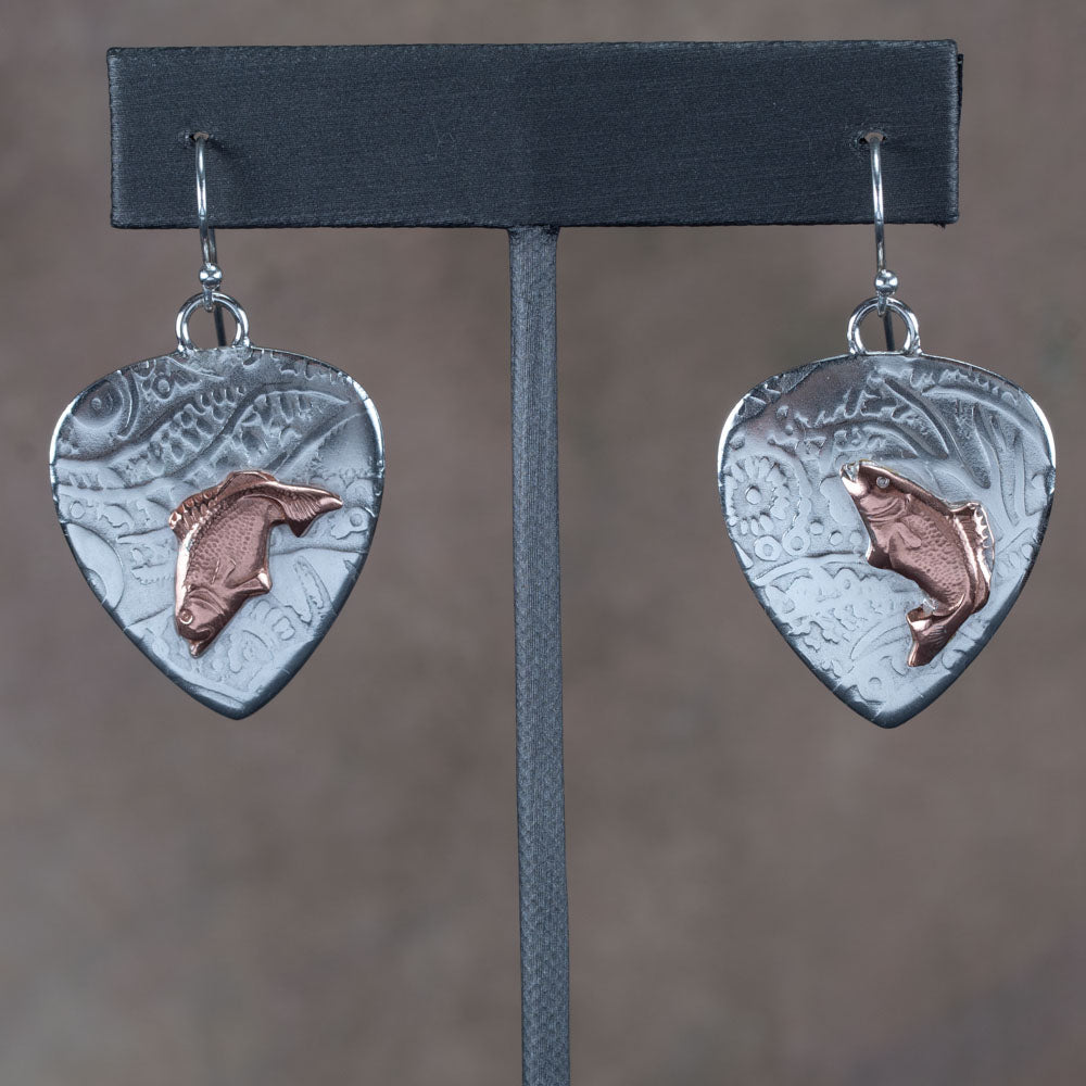 Handcrafted mixed metal earrings featuring copper jumping bass fish on textured fine silver backdrops with nature-inspired patterns – Gone Fishin’ earrings by Divella Designs, displayed on earthy background.