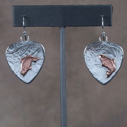 Handcrafted mixed metal earrings featuring copper jumping bass fish on textured fine silver backdrops with nature-inspired patterns – Gone Fishin’ earrings by Divella Designs, displayed on earthy background.