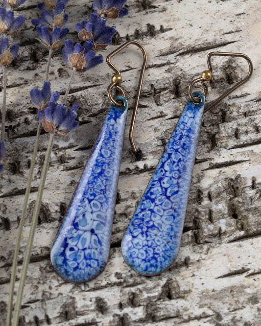 Handcrafted enamel teardrop earrings in ocean-inspired blue and white pattern, displayed on birch bark with dried lavender – Moonlit Tide design by Divella Design.