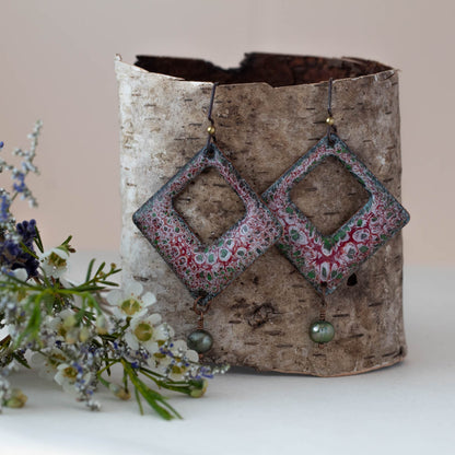 Handmade enamel earrings with red, green, and white floral pattern – diamond-shaped dangle earrings with open center and green pearl accent, artisan jewelry by Divella Designs.