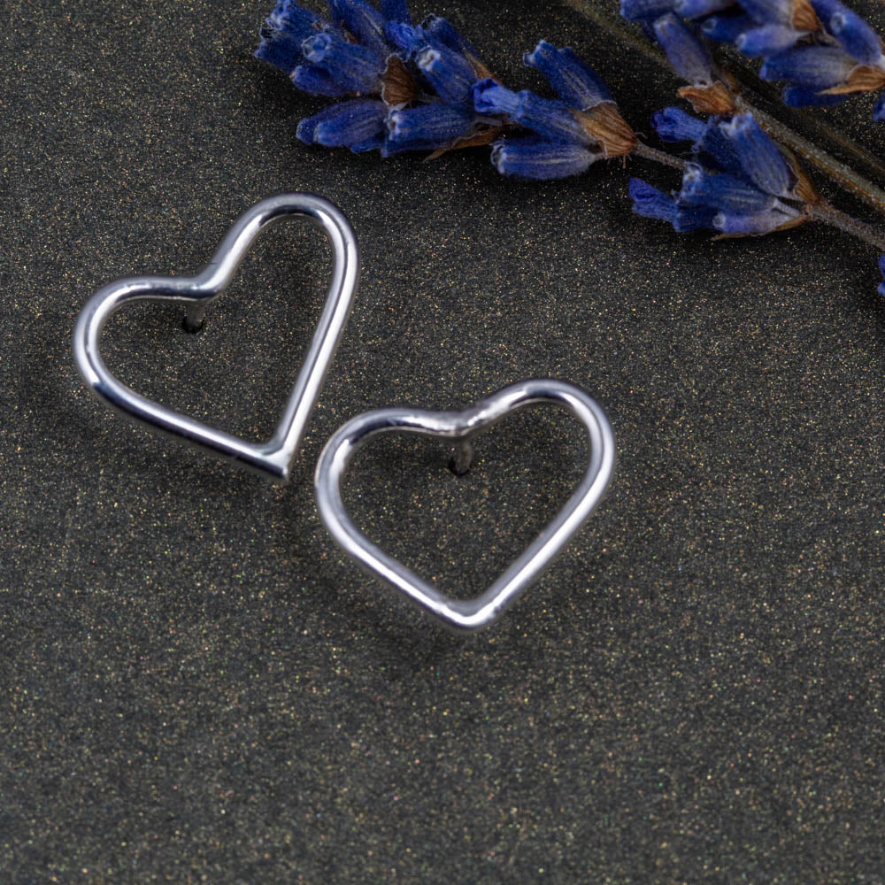 Heart-shaped silver earrings on a dark surface with lavender flowers.