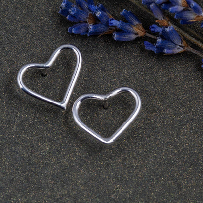 Heart-shaped silver earrings on a dark surface with lavender flowers.