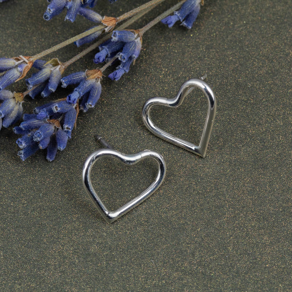 Silver heart-shaped earrings on a dark surface with lavender flowers.