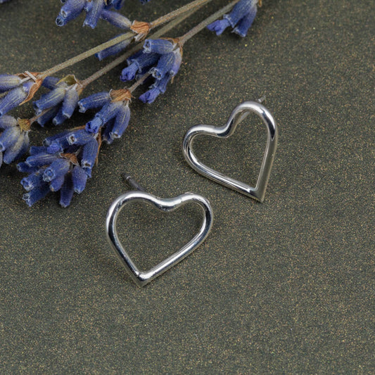 Silver heart-shaped earrings on a dark surface with lavender flowers.