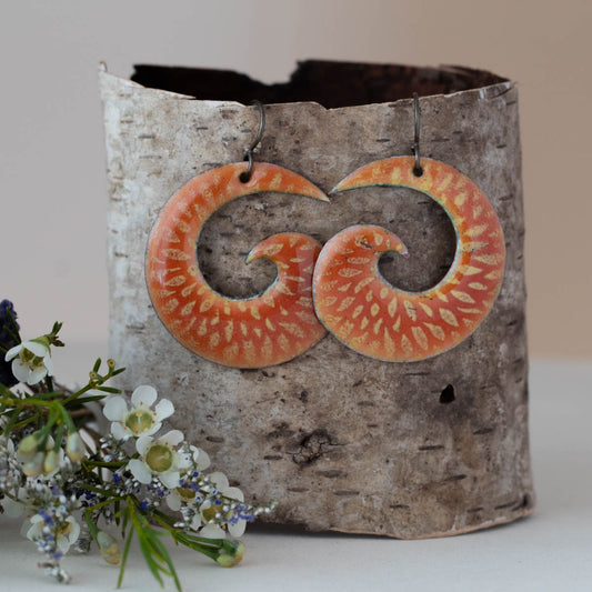 Bright orange and yellow spiral enamel earrings with sunburst floral pattern, nature-inspired artisan jewelry by Divella Designs."