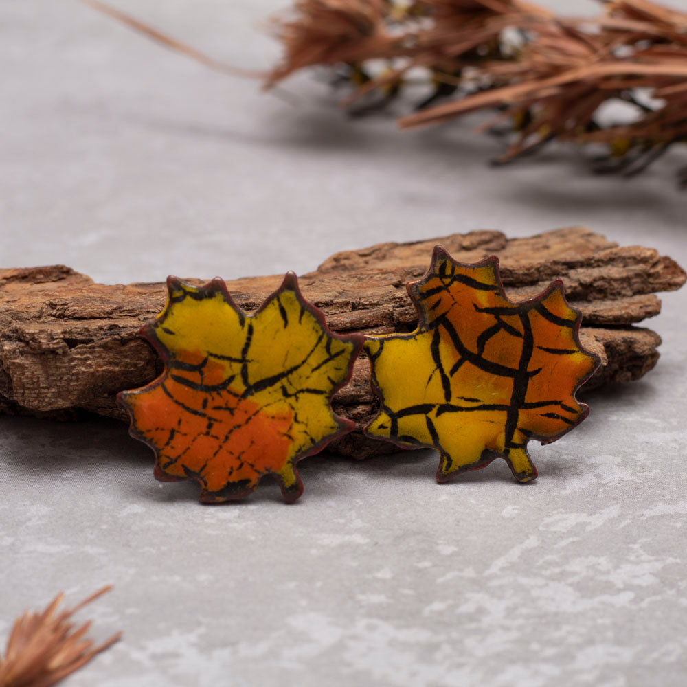 Two maple leaf-shaped pins with a cracked glass effect on a wooden surface.