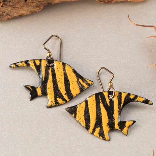 Handmade enamel fish-shaped earrings in bold orange and black stripes, styled with driftwood and natural textures – artisan jewelry by Divella Designs
