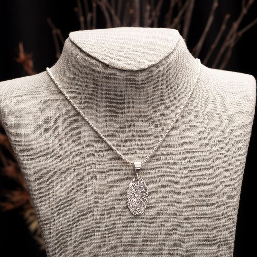 Sterling silver oval pendant necklace with textured landscape design on 18-inch chain.
