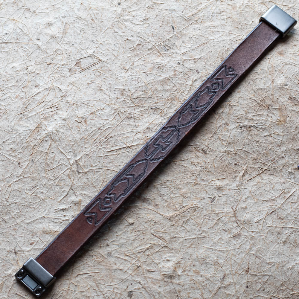 Brown leather bracelet with embossed design on a beige surface