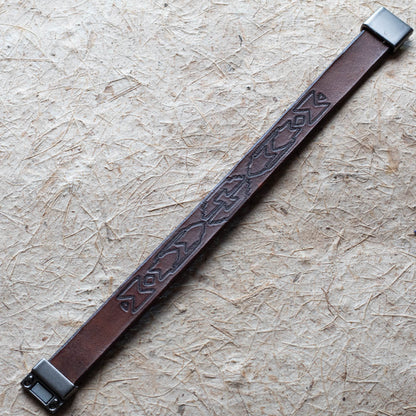 Brown leather bracelet with embossed design on a beige surface