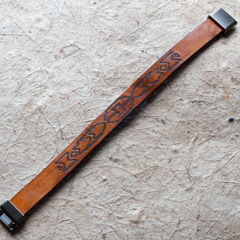 Brown leather bracelet with embossed design on a textured beige surface