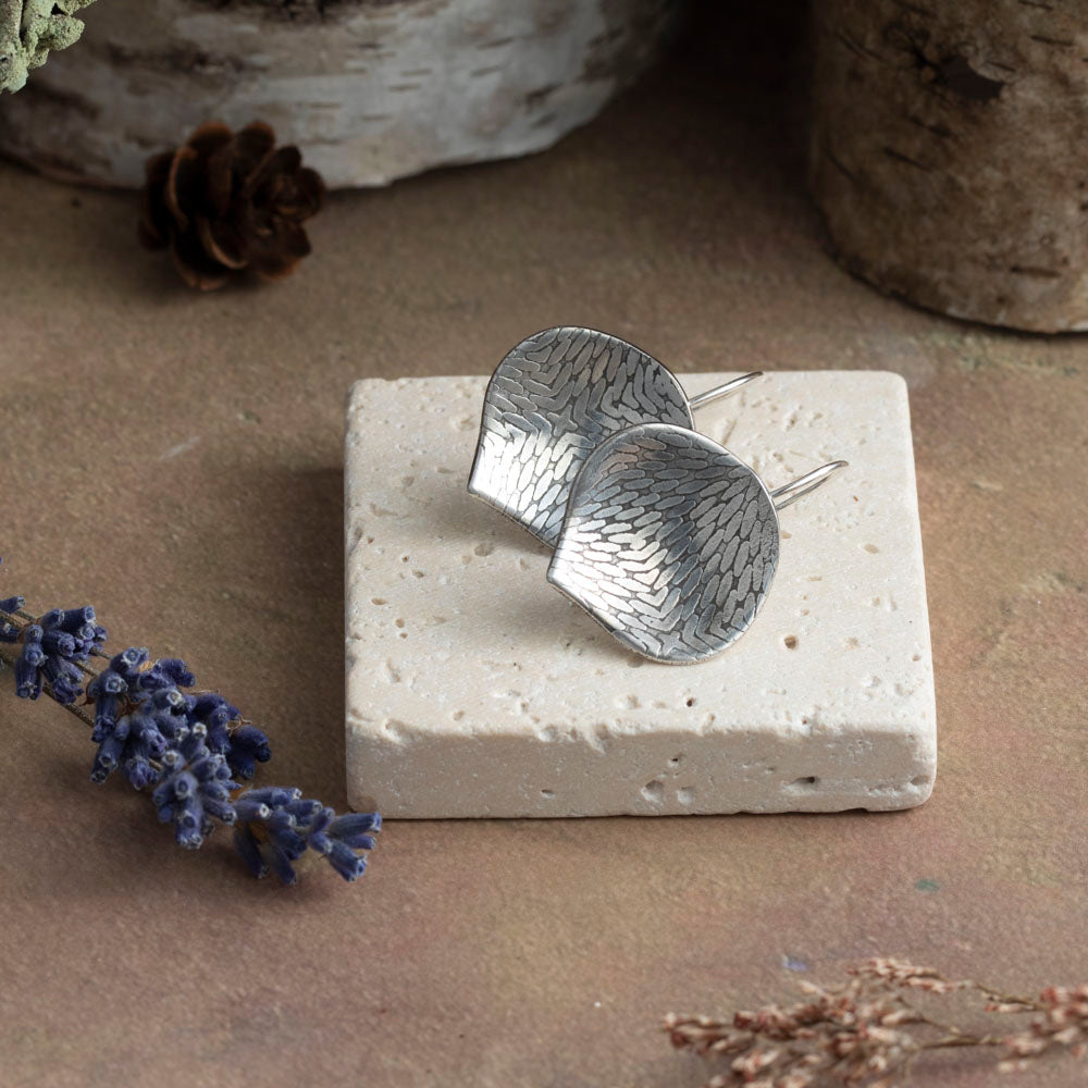 Silver earrings on a stone block with natural elements in the background