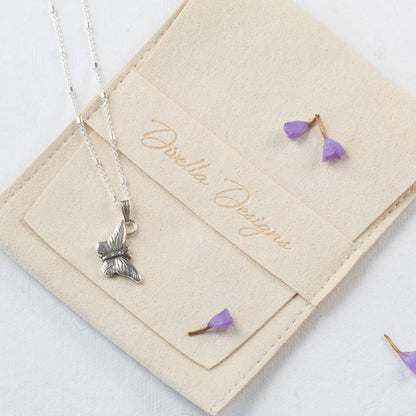 Delicate sterling silver butterfly pendant necklace with fine wing detailing, displayed on a branded pouch with purple petals.