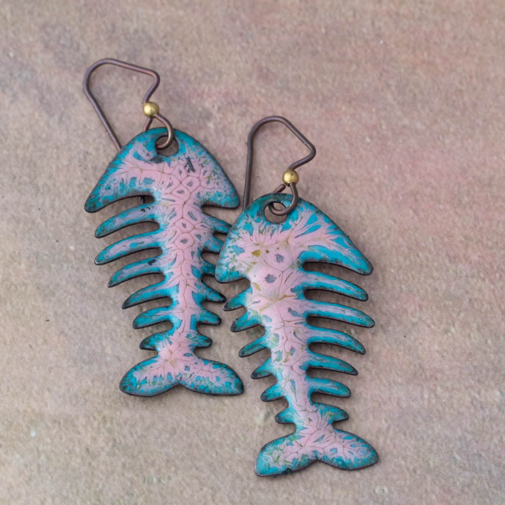 Pair of fish-shaped earrings with blue and pink design on a textured beige background